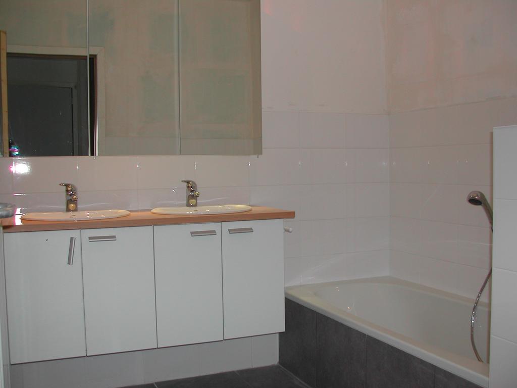 A large bathroom with a bathtub, handheld shower, double sinks, and a mirrored cabinet above the vanity.