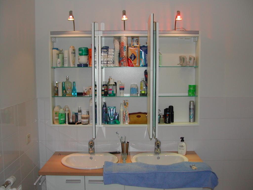 A bathroom with two sinks, a mirror cabinet filled with toiletries, and a blue towel on the counter.