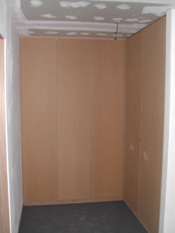 Built-in wooden wardrobes in a bedroom, with unfinished ceiling and walls, photographed before moving in March 2003.