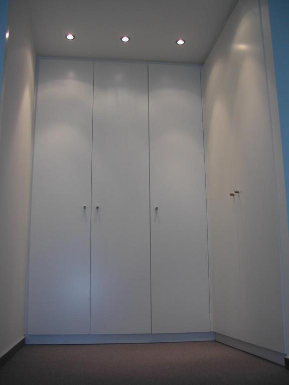 White built-in wardrobe with four doors in a bedroom, illuminated by three ceiling lights.