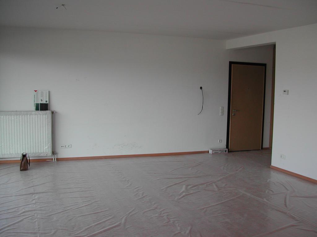 Empty living room with plastic covering the floor, a radiator on the wall, and a closed door in the background.