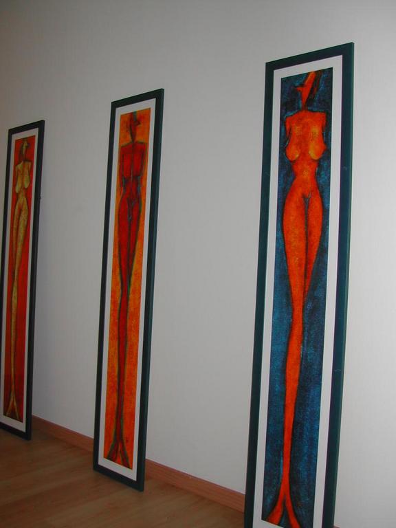 Three tall, narrow framed paintings of abstract human figures lean against a white wall in a living room.
