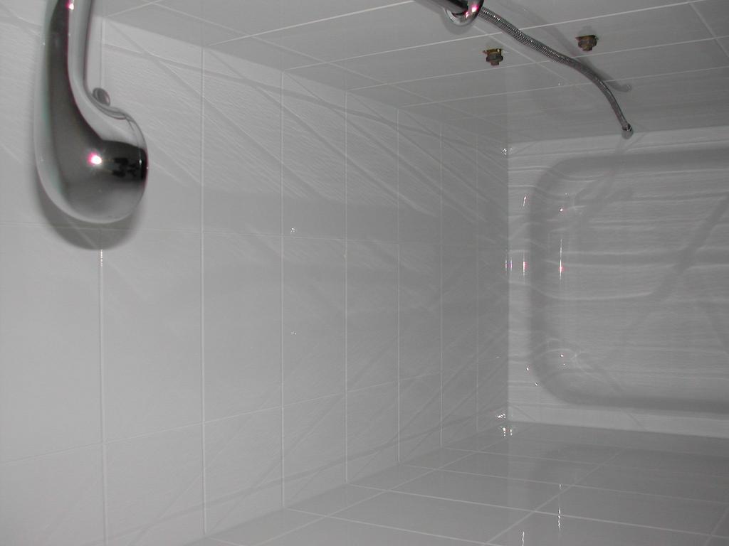 A small bathroom with white tiled walls, a shower area, and a metal grab bar on the wall.