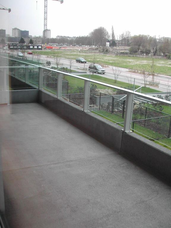 A spacious apartment terrace with a glass railing, overlooking a road and green area, taken before moving in 2003.