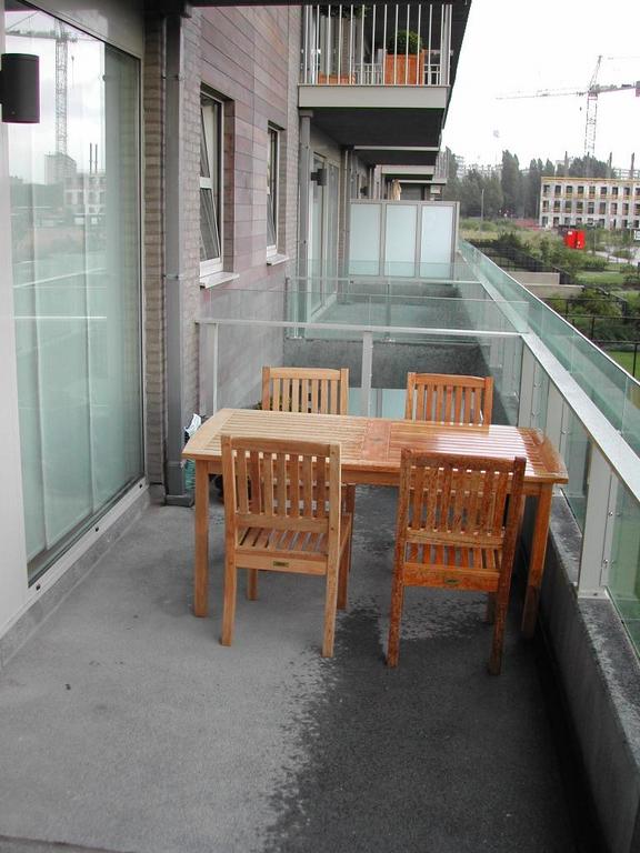 A wooden table with four chairs on a balcony, partially wet from rain while the other part remains dry.