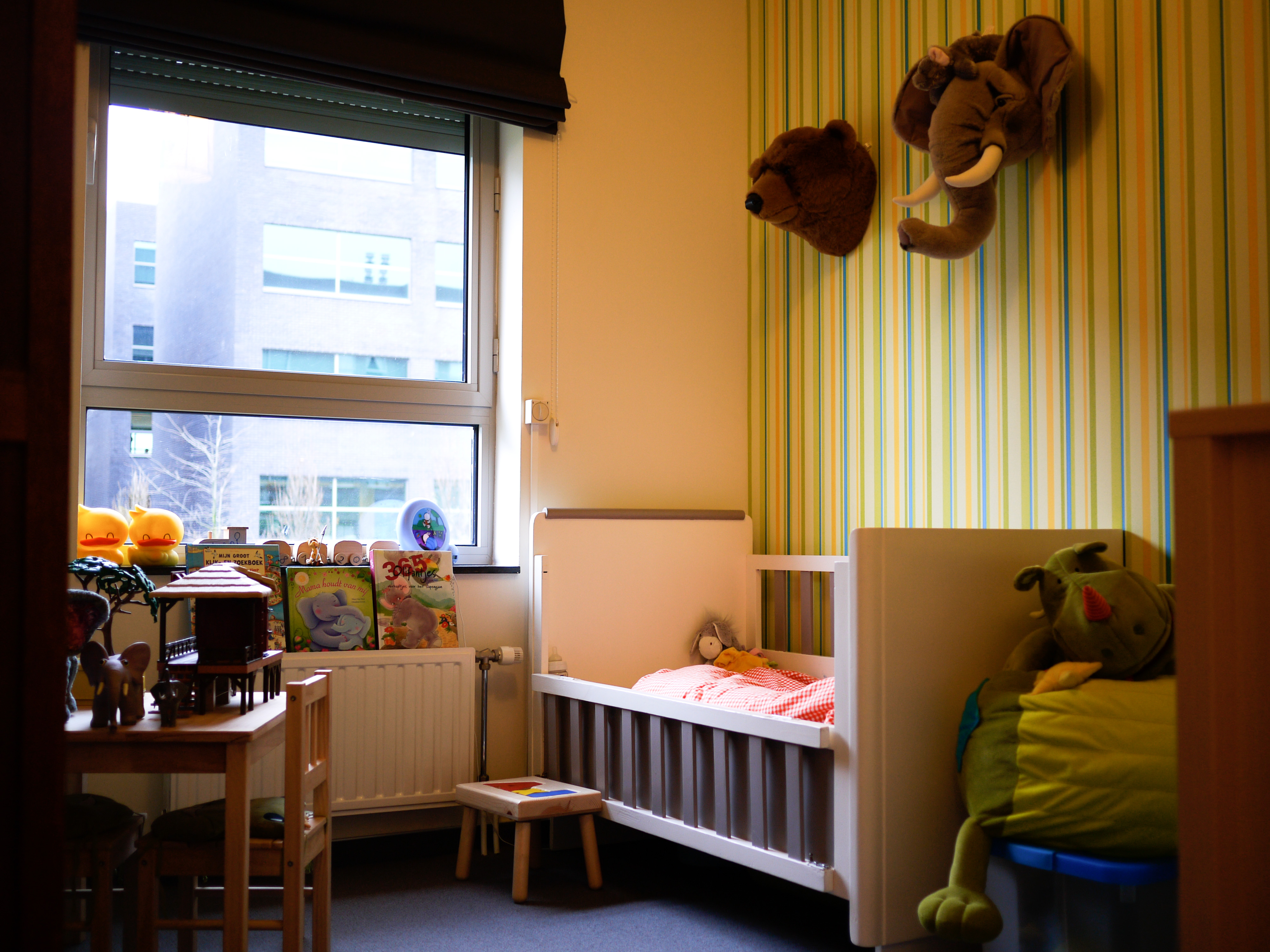 A children's bedroom with a crib, stuffed animals, books, and a small table with chairs near the window.