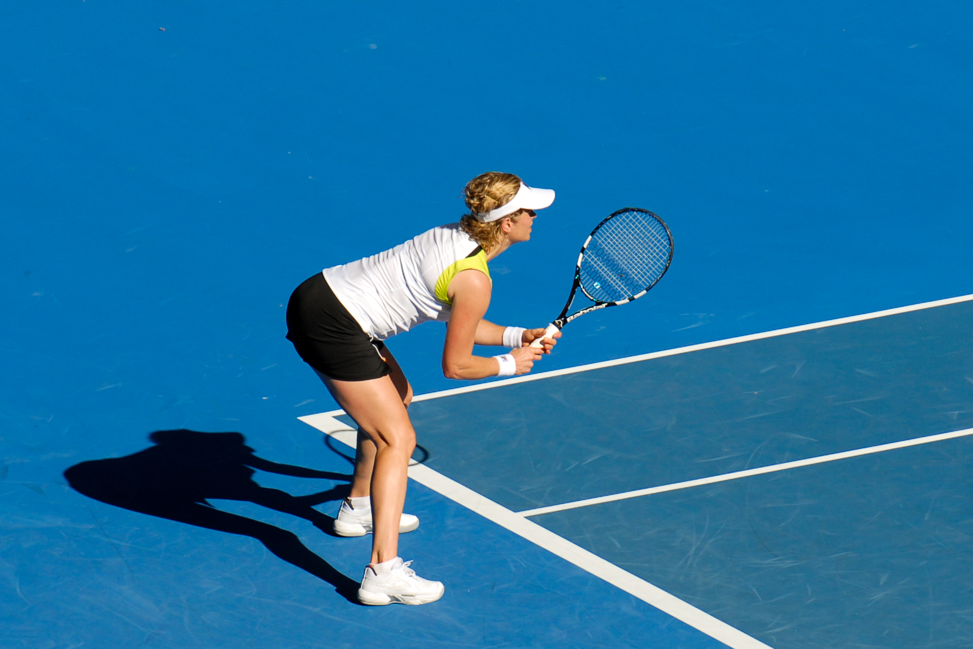 A tennis player in a ready position, holding a racket, preparing to receive a serve on a blue court.