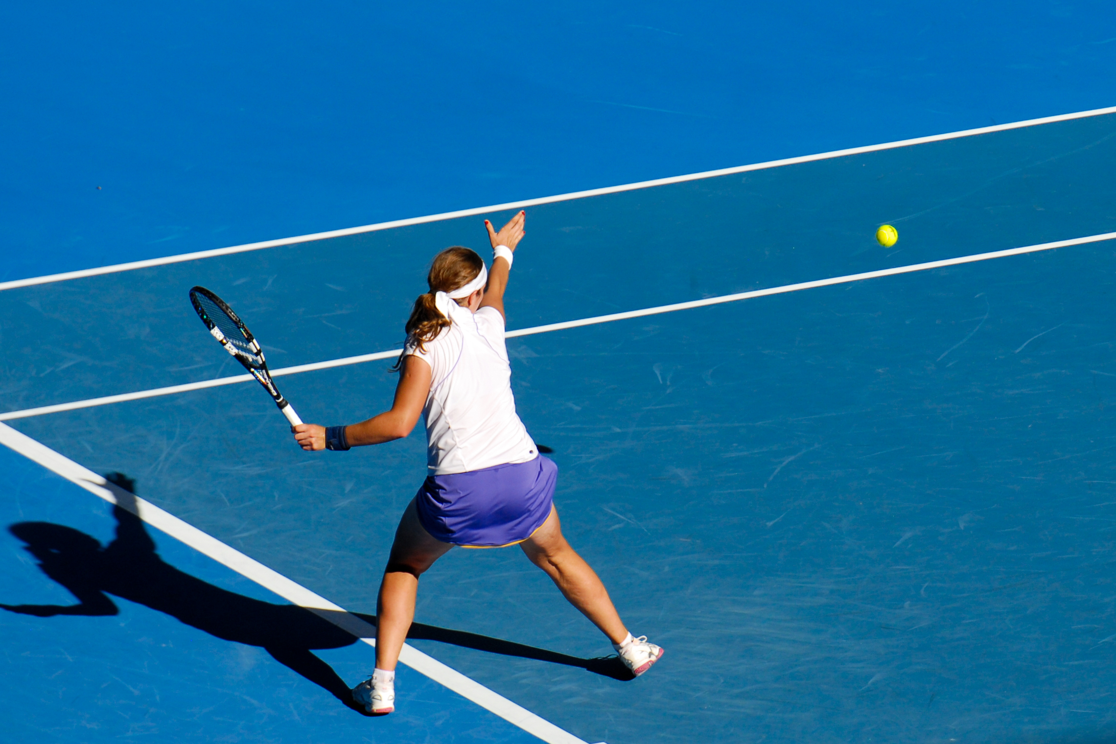 A tennis player in a white and purple outfit prepares to hit a forehand shot on a blue court.