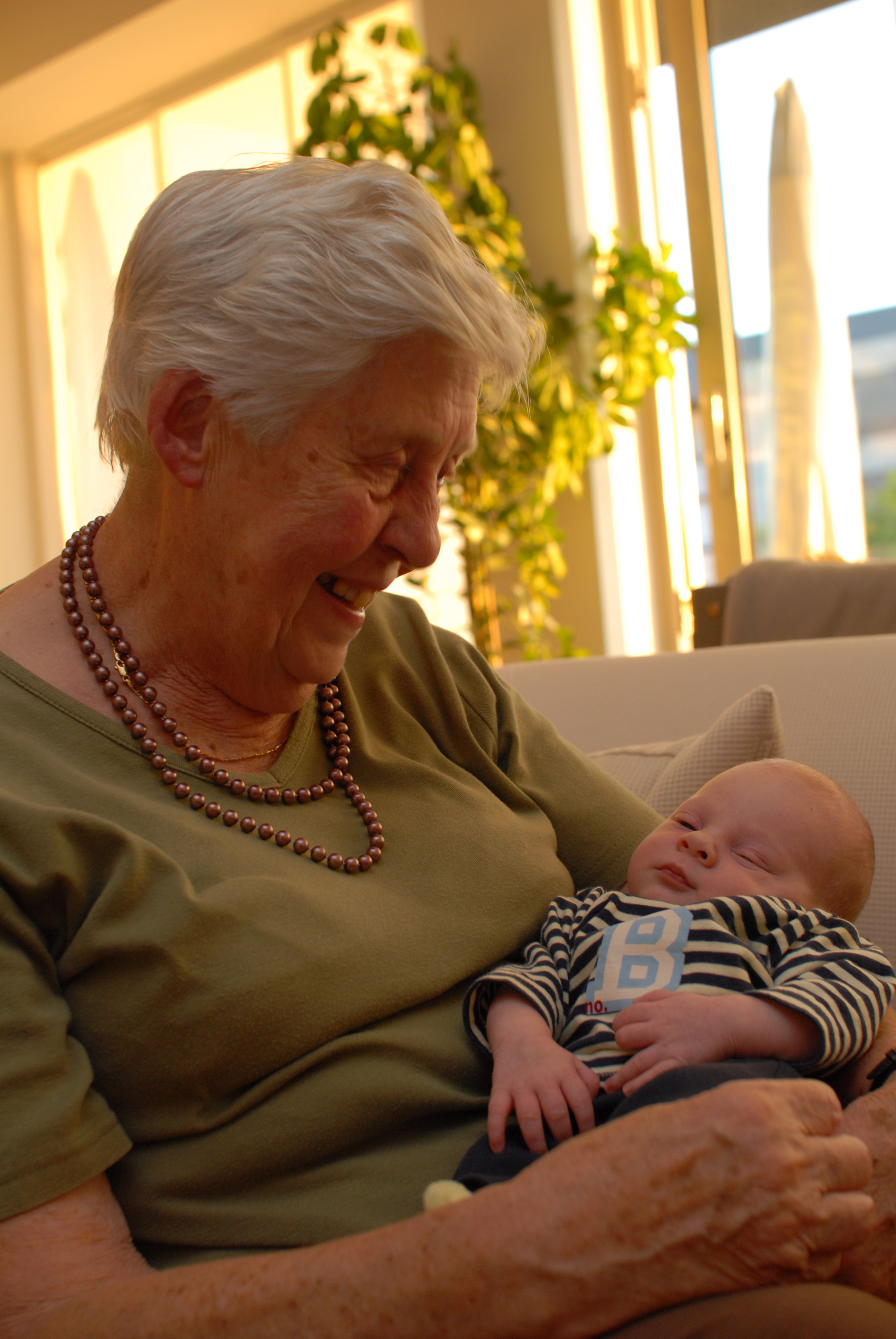 An elderly woman smiles while holding a sleeping baby in her arms.