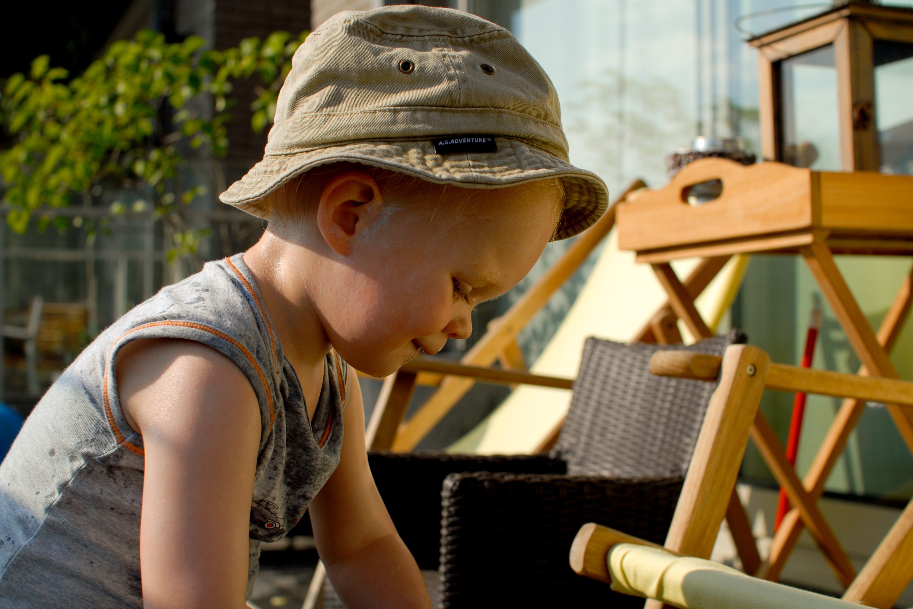 A young child wearing a hat and sleeveless shirt plays on a terrace, focused on an activity.