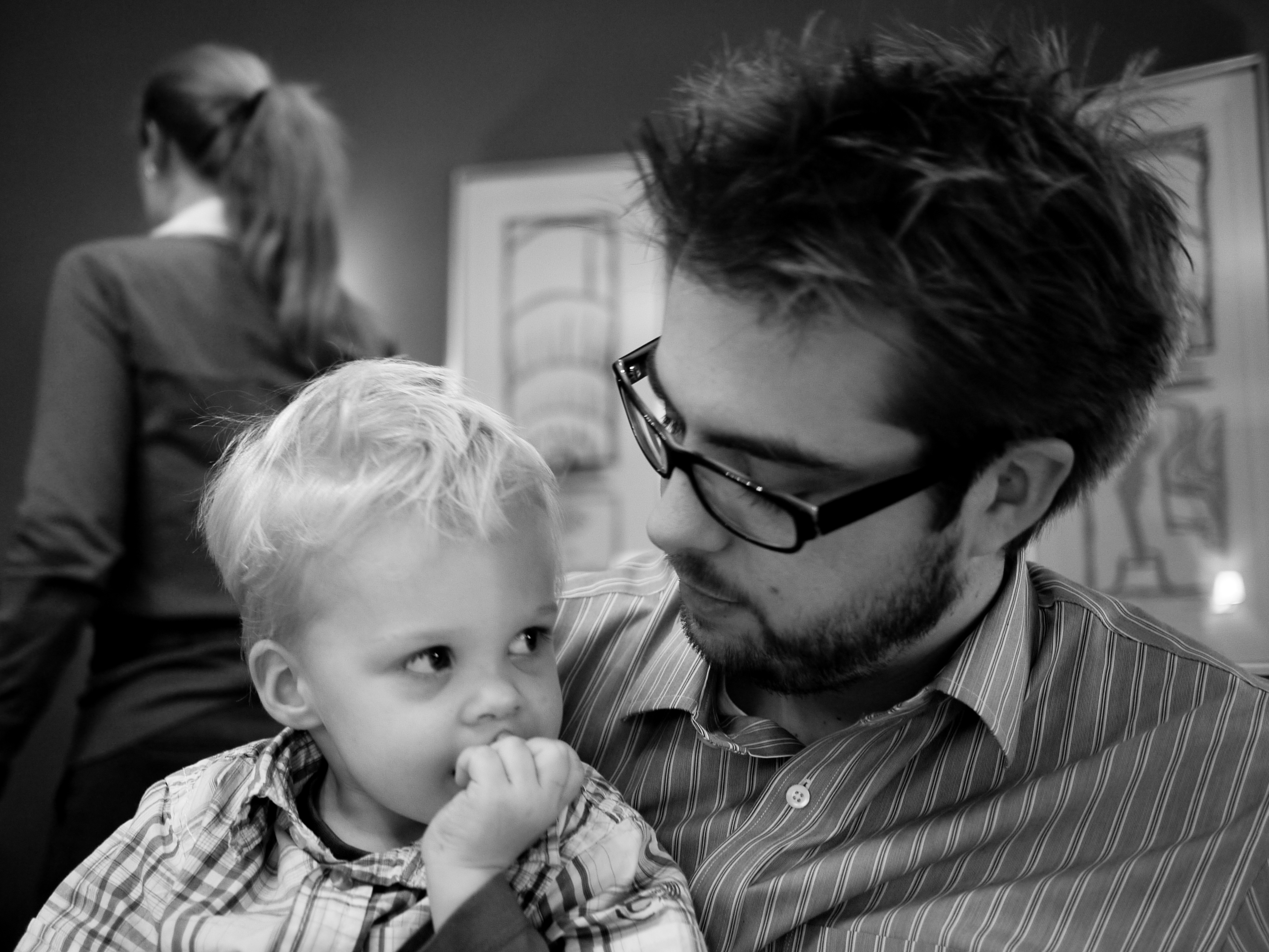 A man wearing glasses looks at a young child who is sucking their thumb.