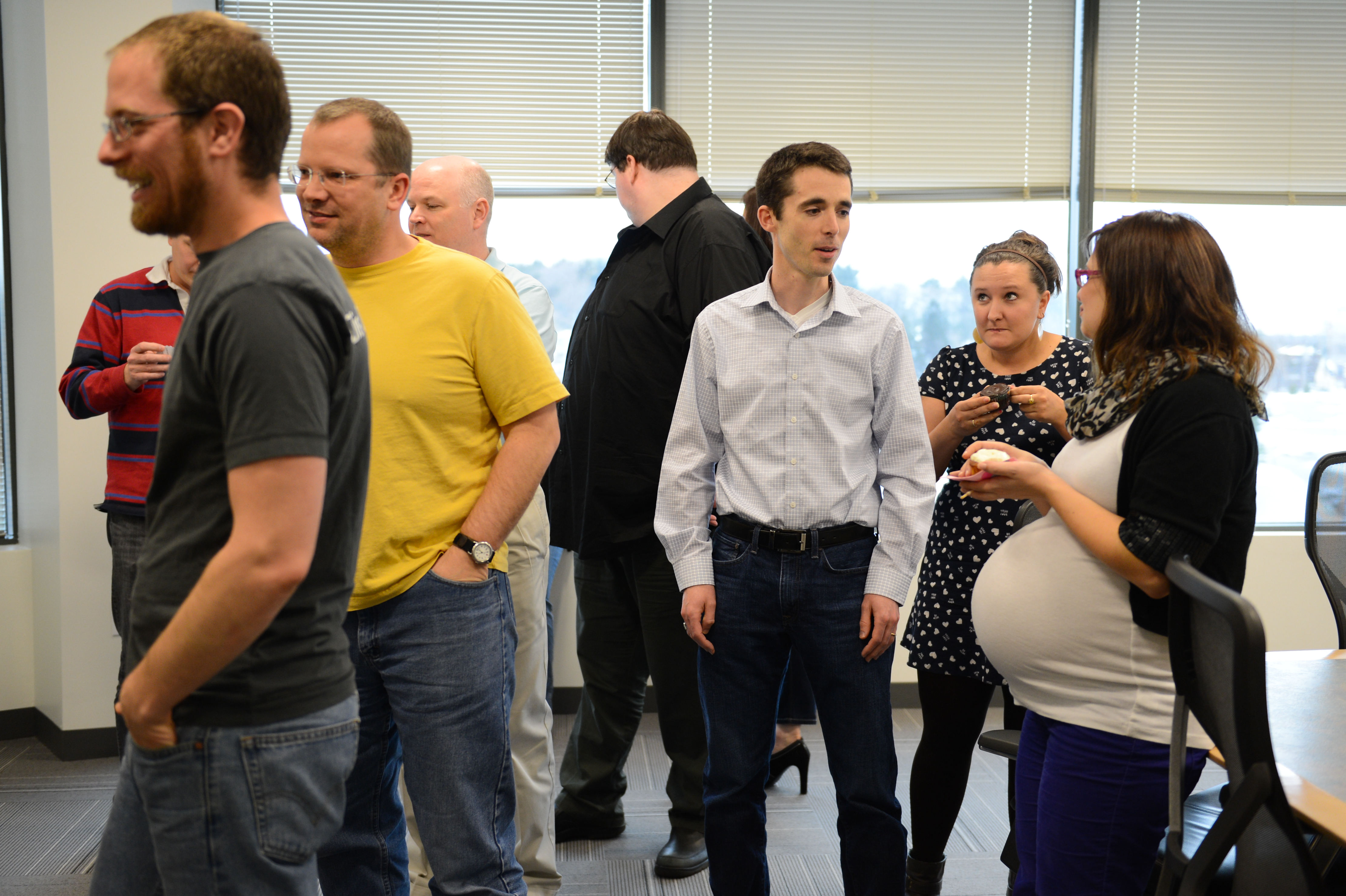 A group of people socializing at a baby shower, with a pregnant woman holding a small plate of food.