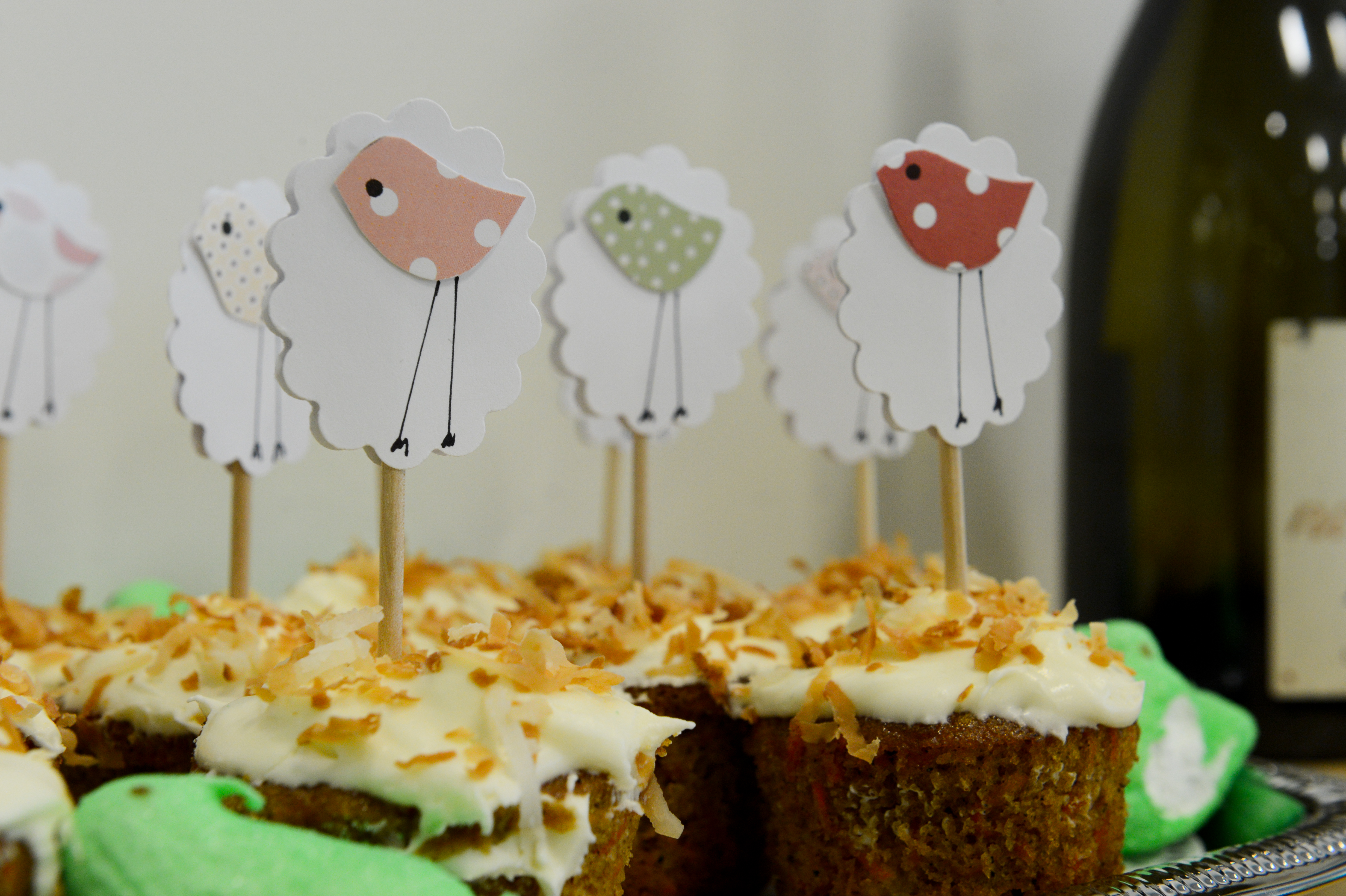 Cupcakes with white frosting and toasted coconut, decorated with sheep-shaped toppers on sticks at a baby shower.