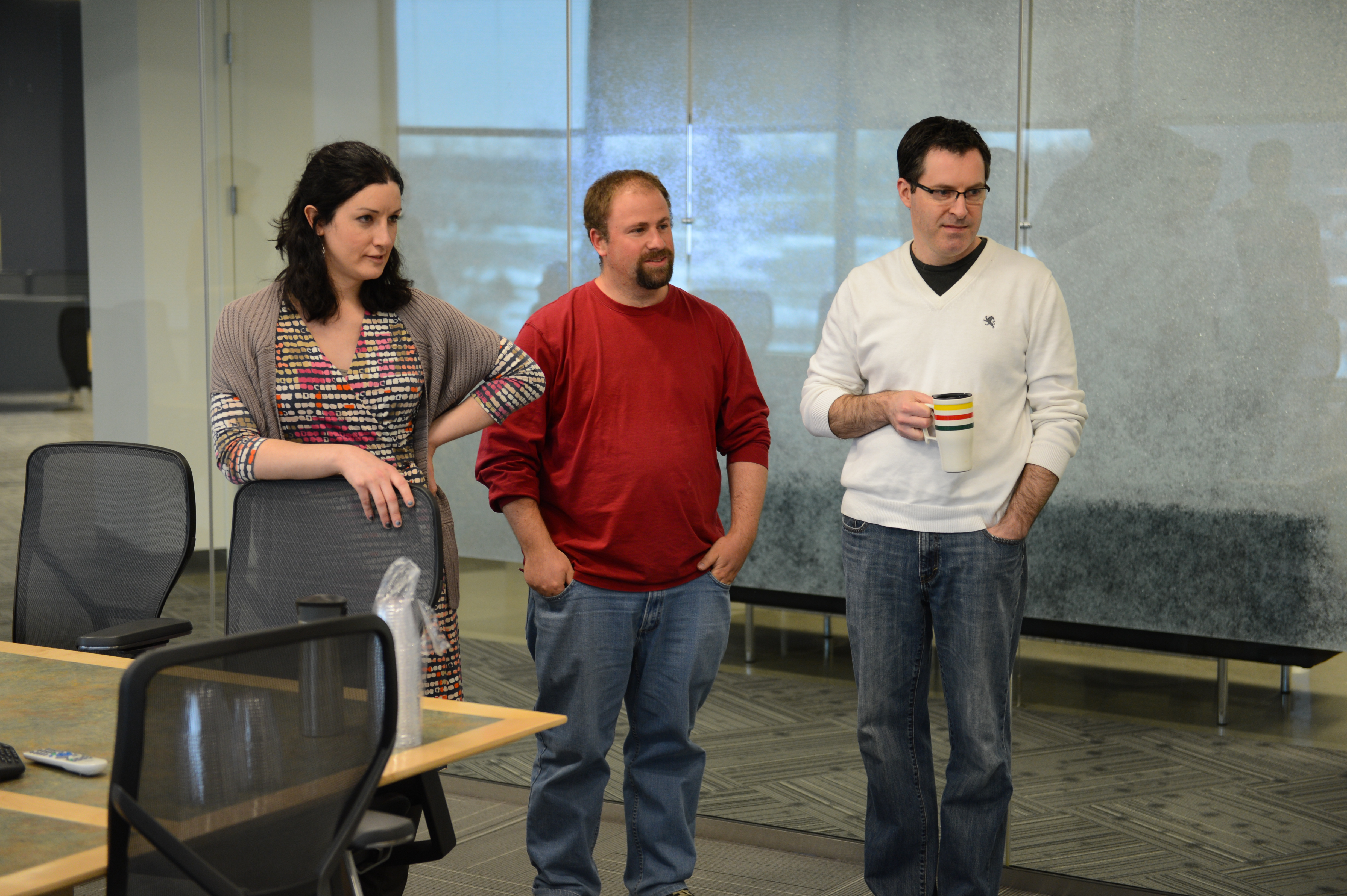Three people stand in an office, engaged in conversation.