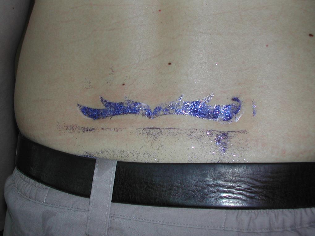A close-up of a person's lower back with a smudged temporary glitter tattoo above their belt.
