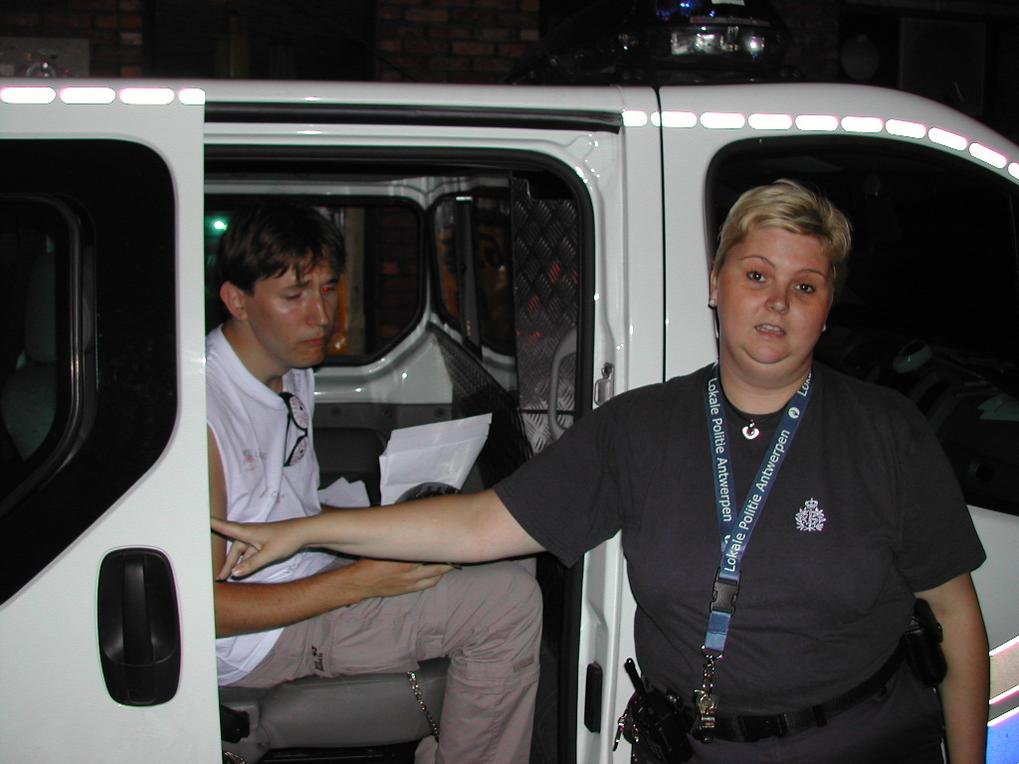 A police officer stands in front of a van while a man sits inside holding papers.