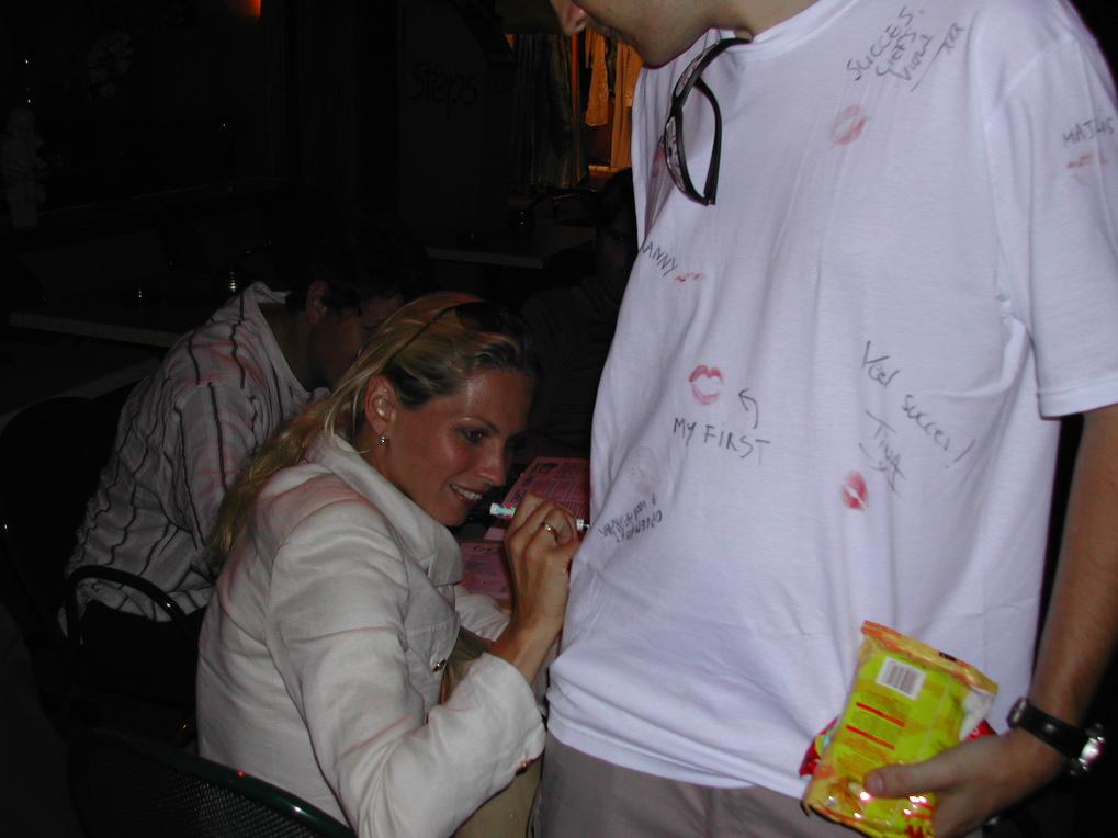 A woman writes on a man's white T-shirt covered in messages and lipstick marks during a celebration.