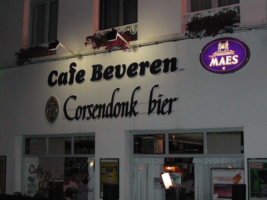 A bar named "Café Beveren" with illuminated signs, viewed from the street during nighttime.