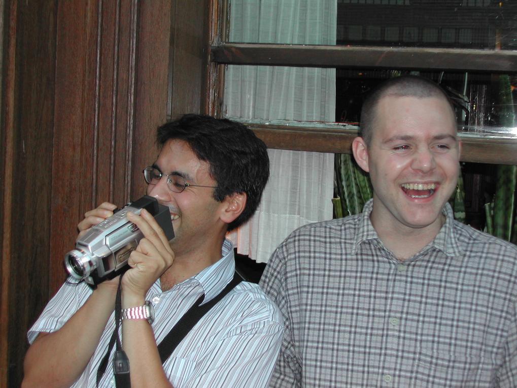 One man laughs while another records with a camcorder during a bachelor party pub crawl.