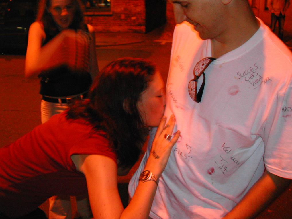 A woman kisses a man's shirt, which has messages and lipstick marks, during a bachelor party pub crawl.