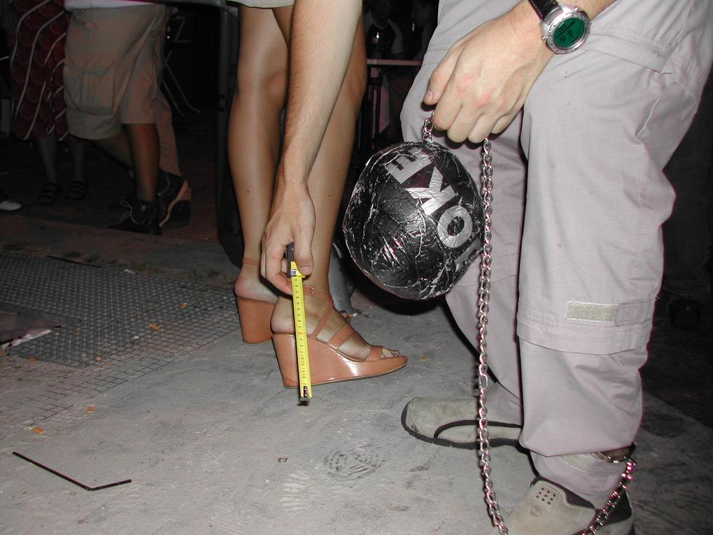 A person in sandals measures heel height while another holds a chained ball labeled "OKÉ" during a night out.