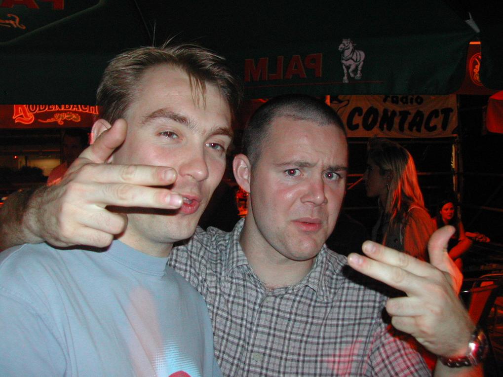 Two men posing at a bar, making playful hand gestures towards the camera.