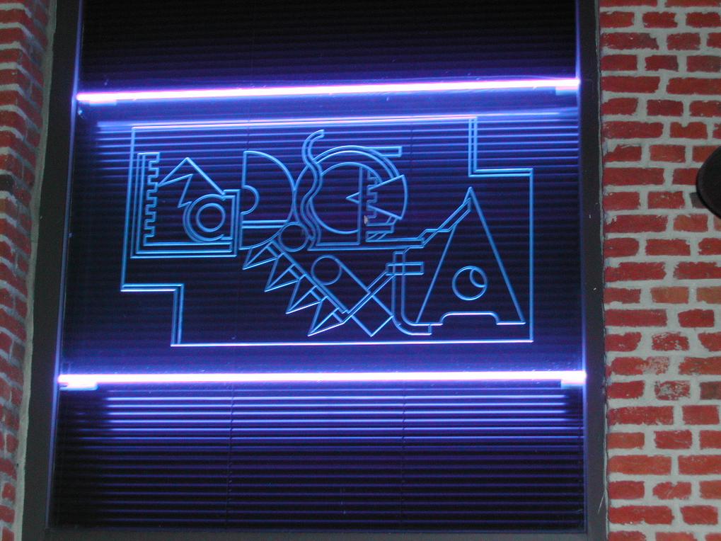 A neon sign with abstract shapes and symbols glows in blue on a brick wall.