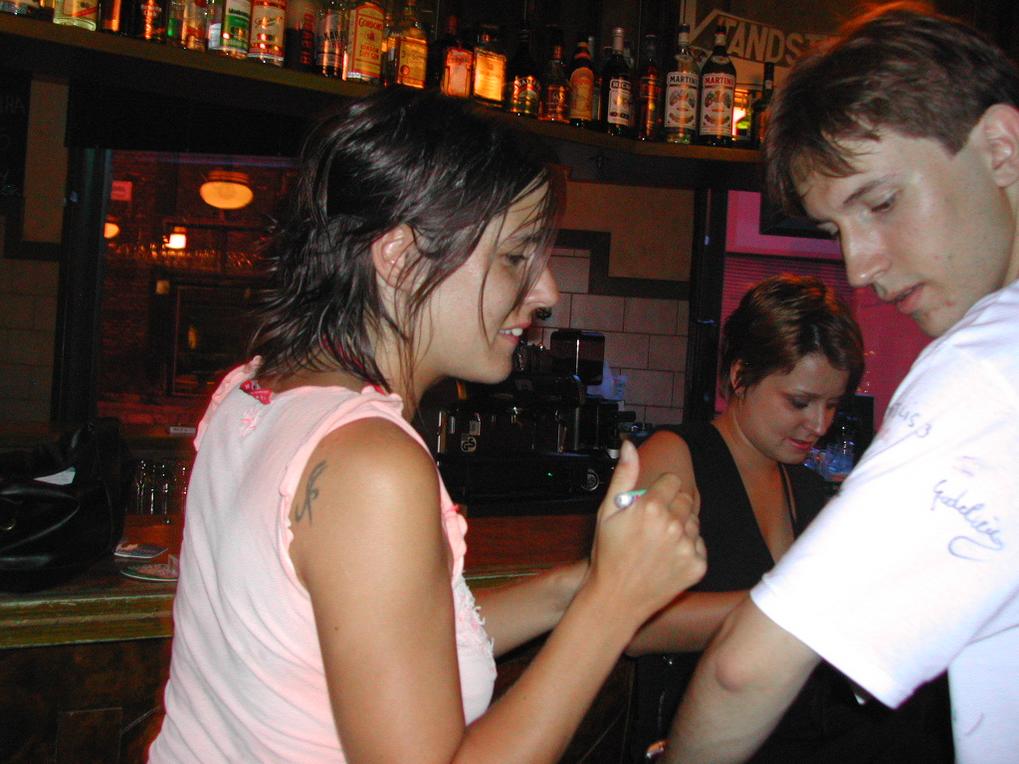 A woman signs a man's white shirt with a marker while another woman stands behind the bar.