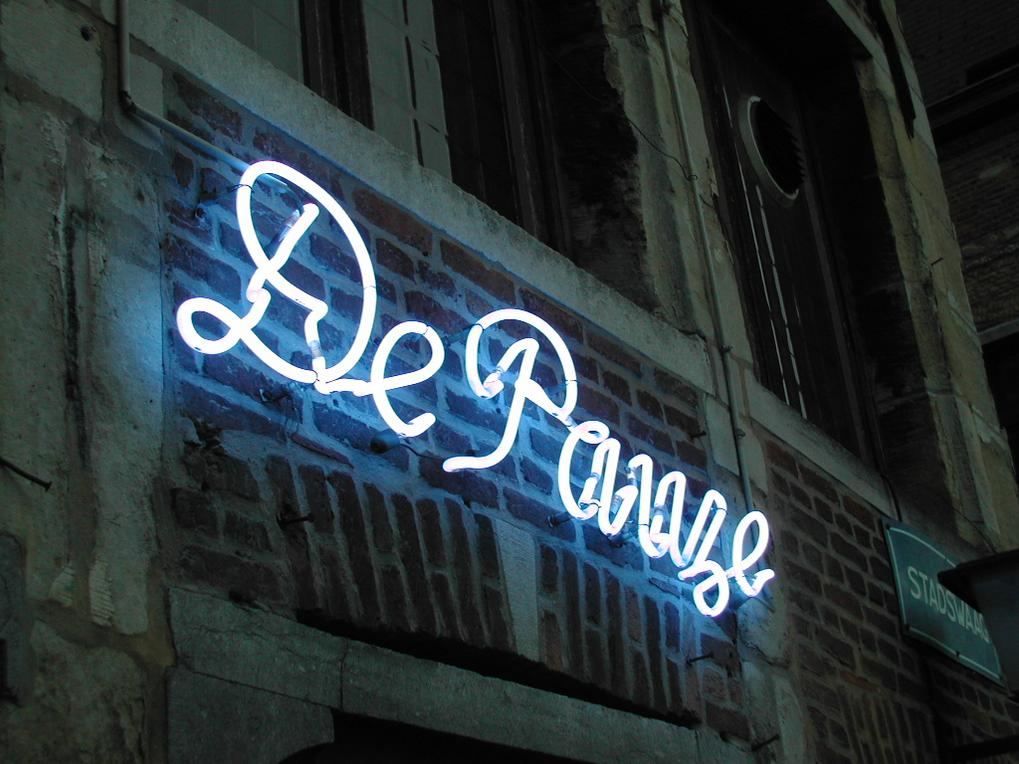 A neon sign reading "De Panne" glows on a brick wall outside a bar at night.