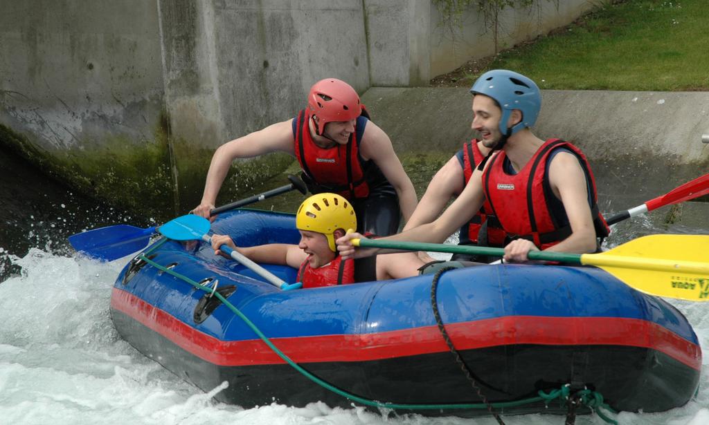 A group of people in helmets and life jackets paddle a blue inflatable raft through whitewater rapids.