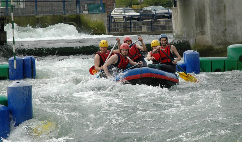 A group of five people wearing helmets and life jackets paddle a raft through whitewater rapids.