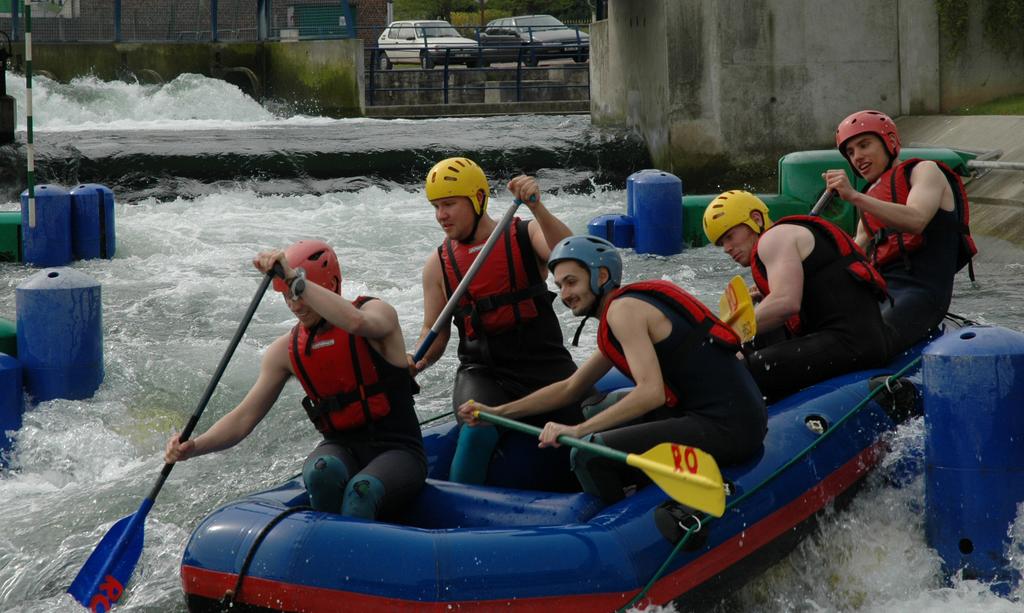Five people in helmets and life jackets paddle a blue inflatable raft through whitewater rapids.