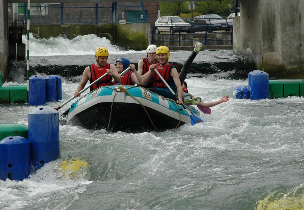 A group of people in helmets and life jackets raft through whitewater, with one person falling overboard.