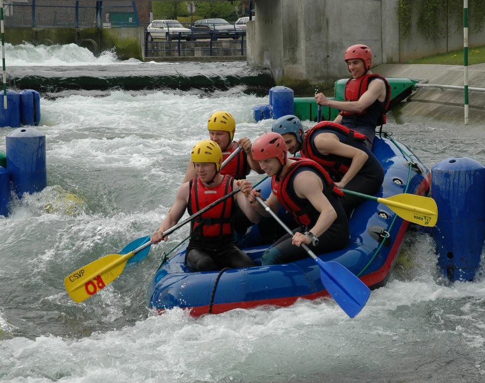 A group of five people in helmets and life jackets paddle a raft through whitewater rapids.