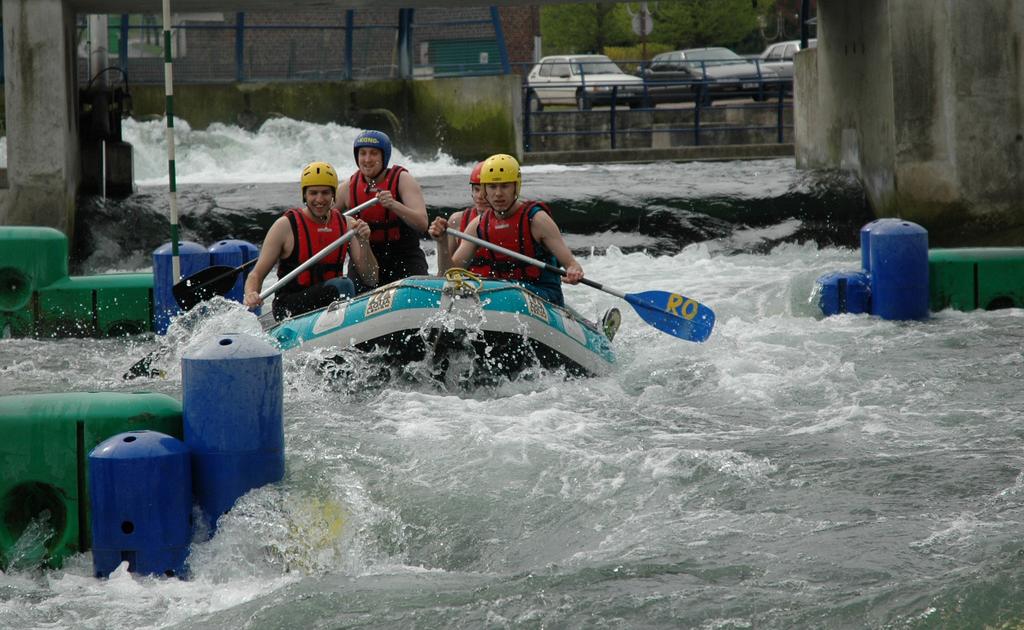 Three people in helmets and life jackets paddle a raft through whitewater rapids on an artificial course.