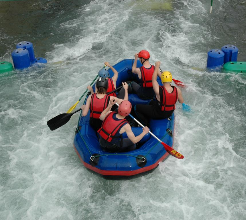 A group of people wearing helmets and life jackets paddle a blue raft through whitewater rapids.