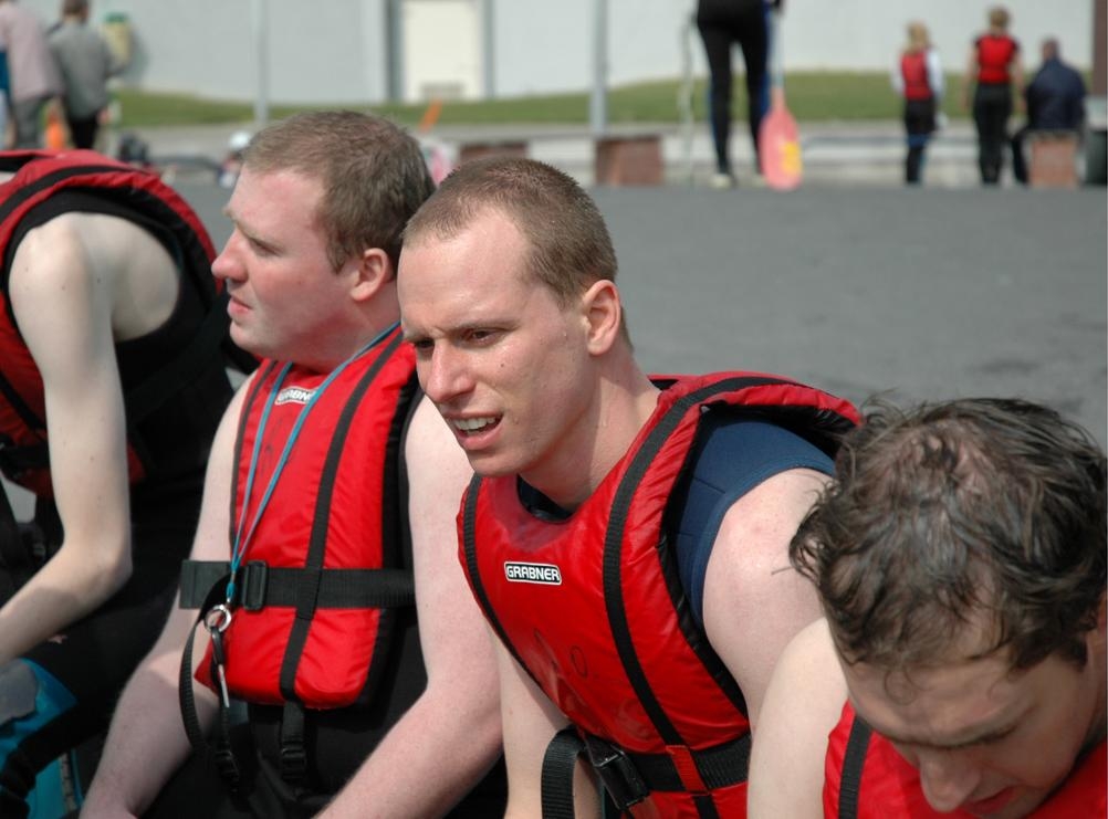 A group of men wearing red life jackets sit together, preparing for an outdoor water activity.