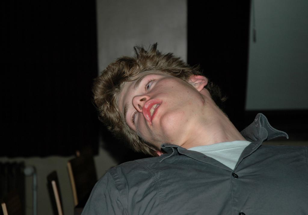 A young man in a gray shirt leans back with his head tilted, mouth slightly open.