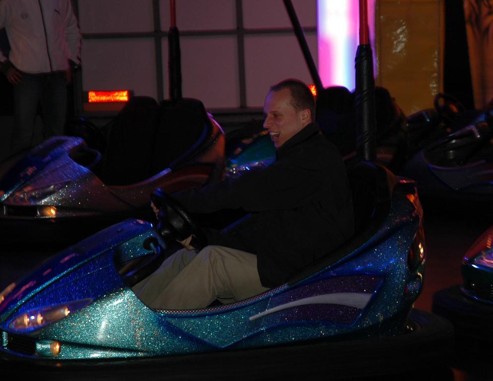 A man smiles while driving a blue bumper car at an indoor amusement venue.