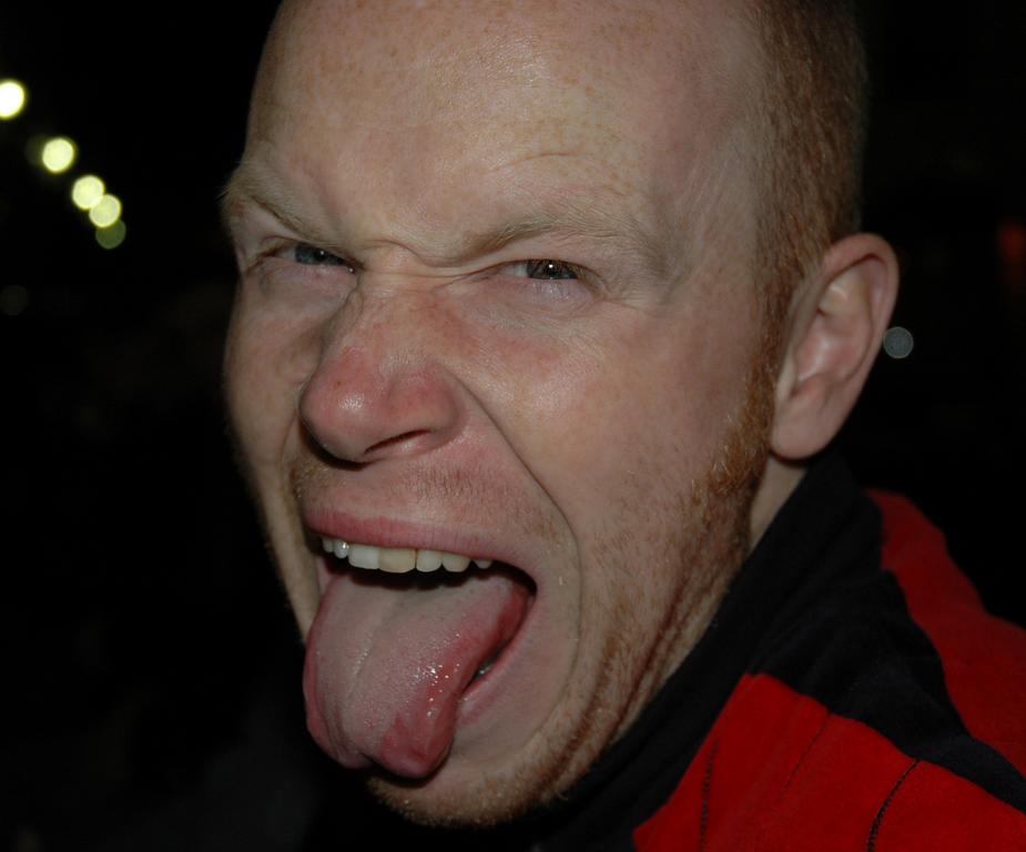 A man in a red and black jacket makes a playful face, sticking out his tongue.