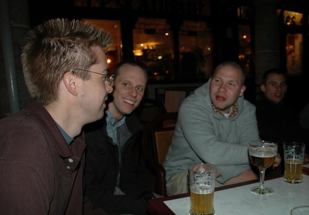 A group of men sitting at a table with beers, engaged in conversation at an outdoor venue.