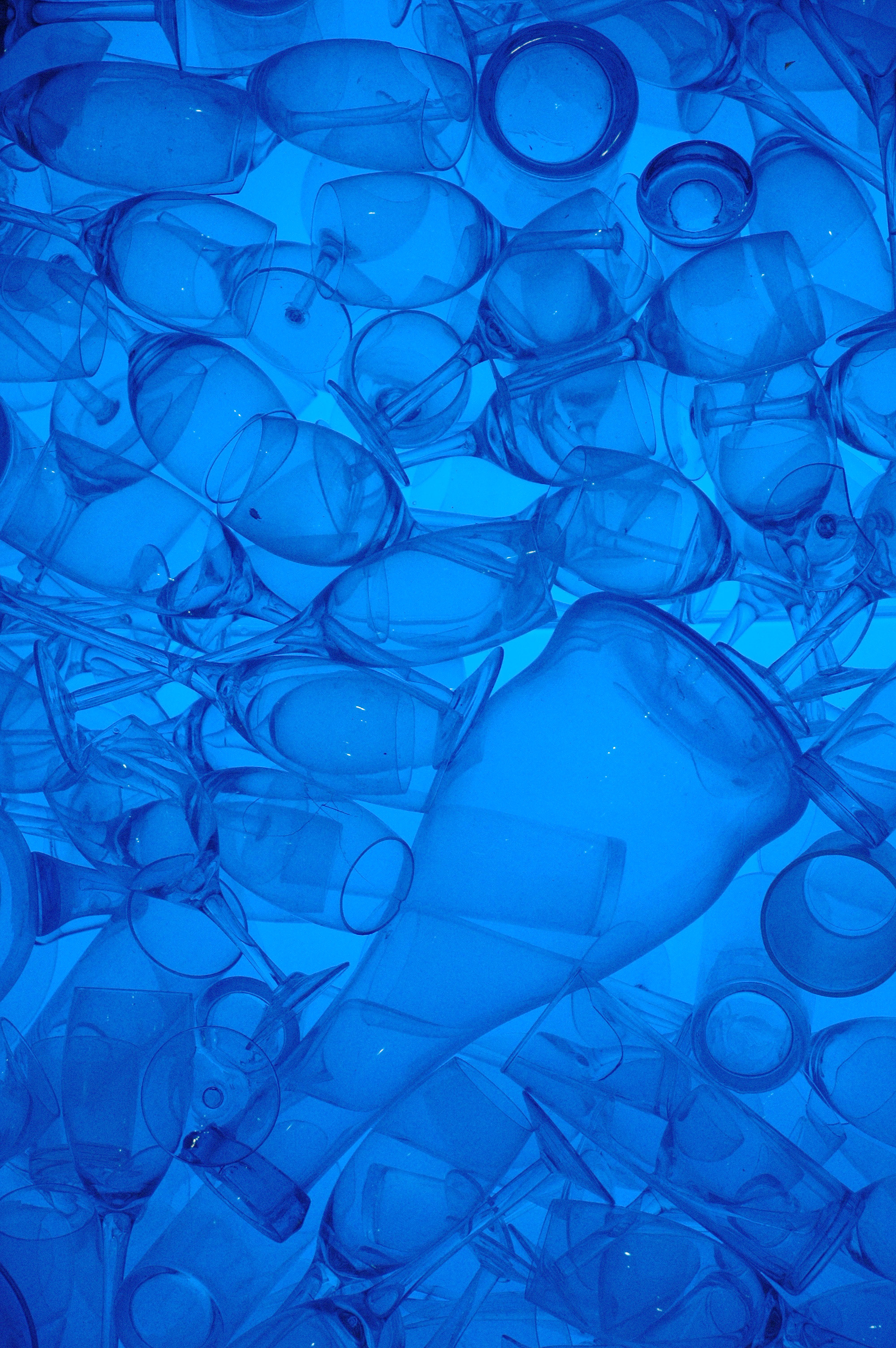 A collection of transparent glass cups and wine glasses stacked together, illuminated by a blue light.