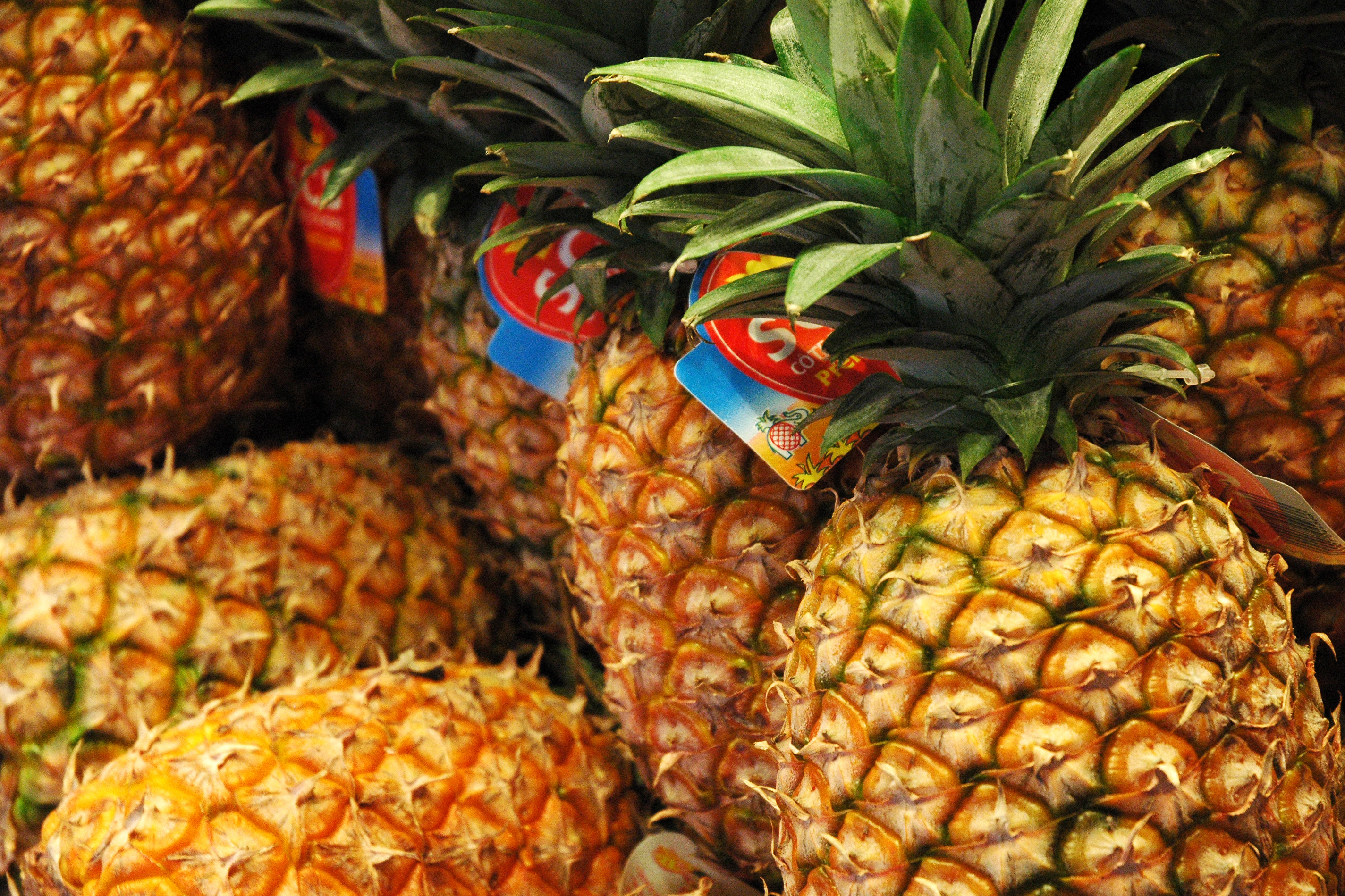 A pile of fresh pineapples with green leaves and price tags at a street market.