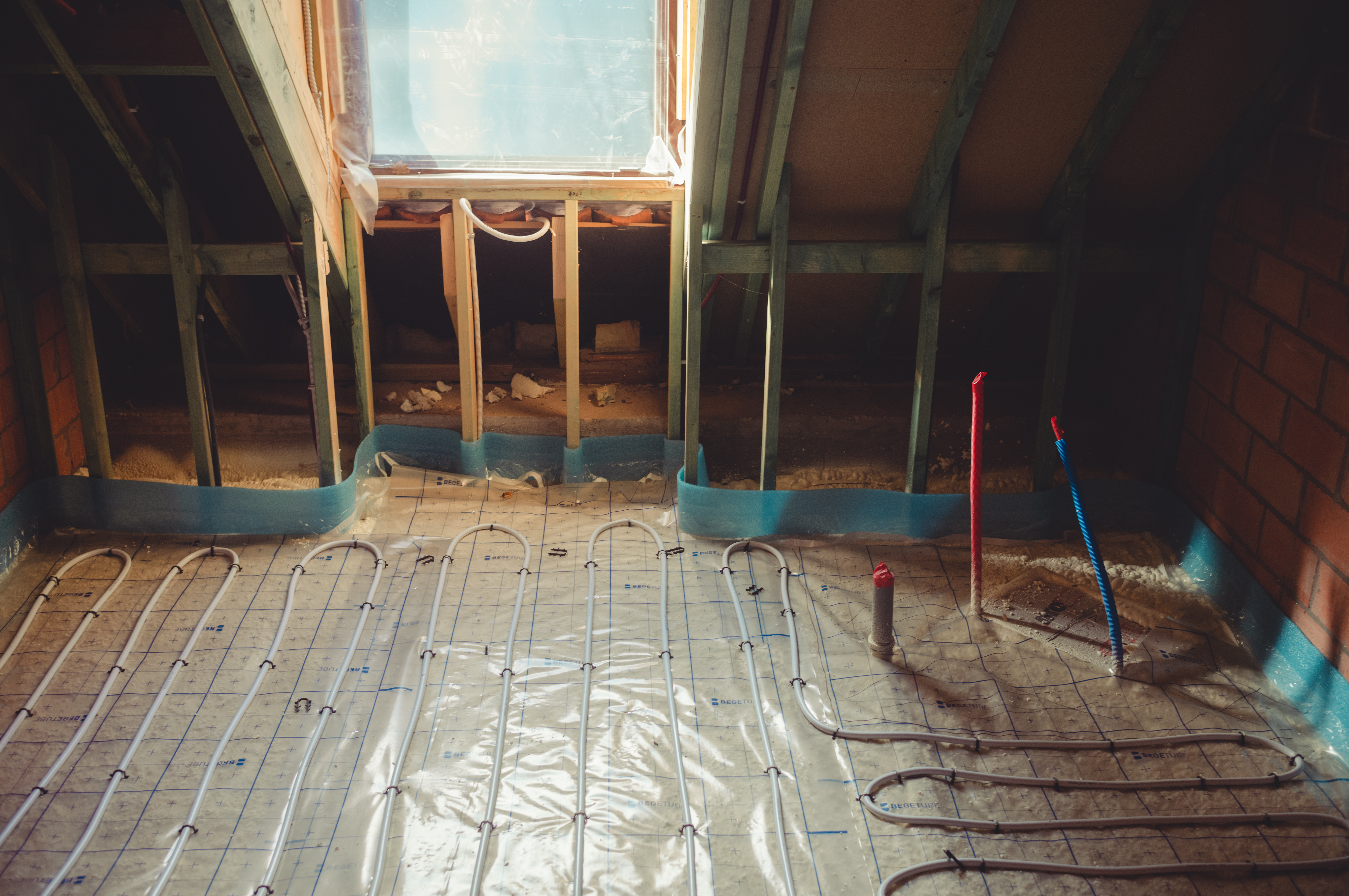 Underfloor heating pipes are being installed in the bathroom, with plumbing connections for the bathtub already in place.