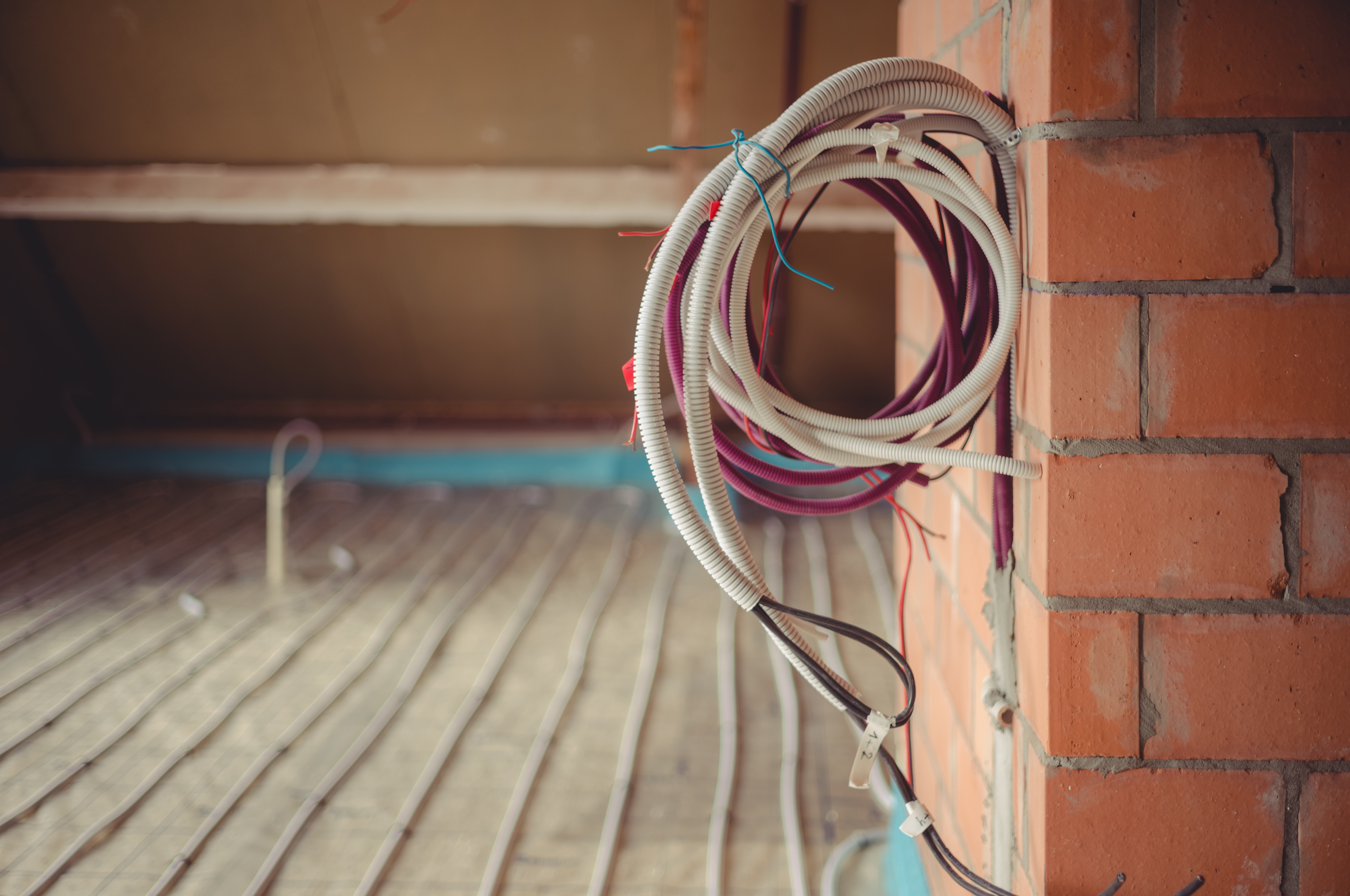 Coiled electrical and communication cables hang on a brick wall, with more cables laid out on the floor.