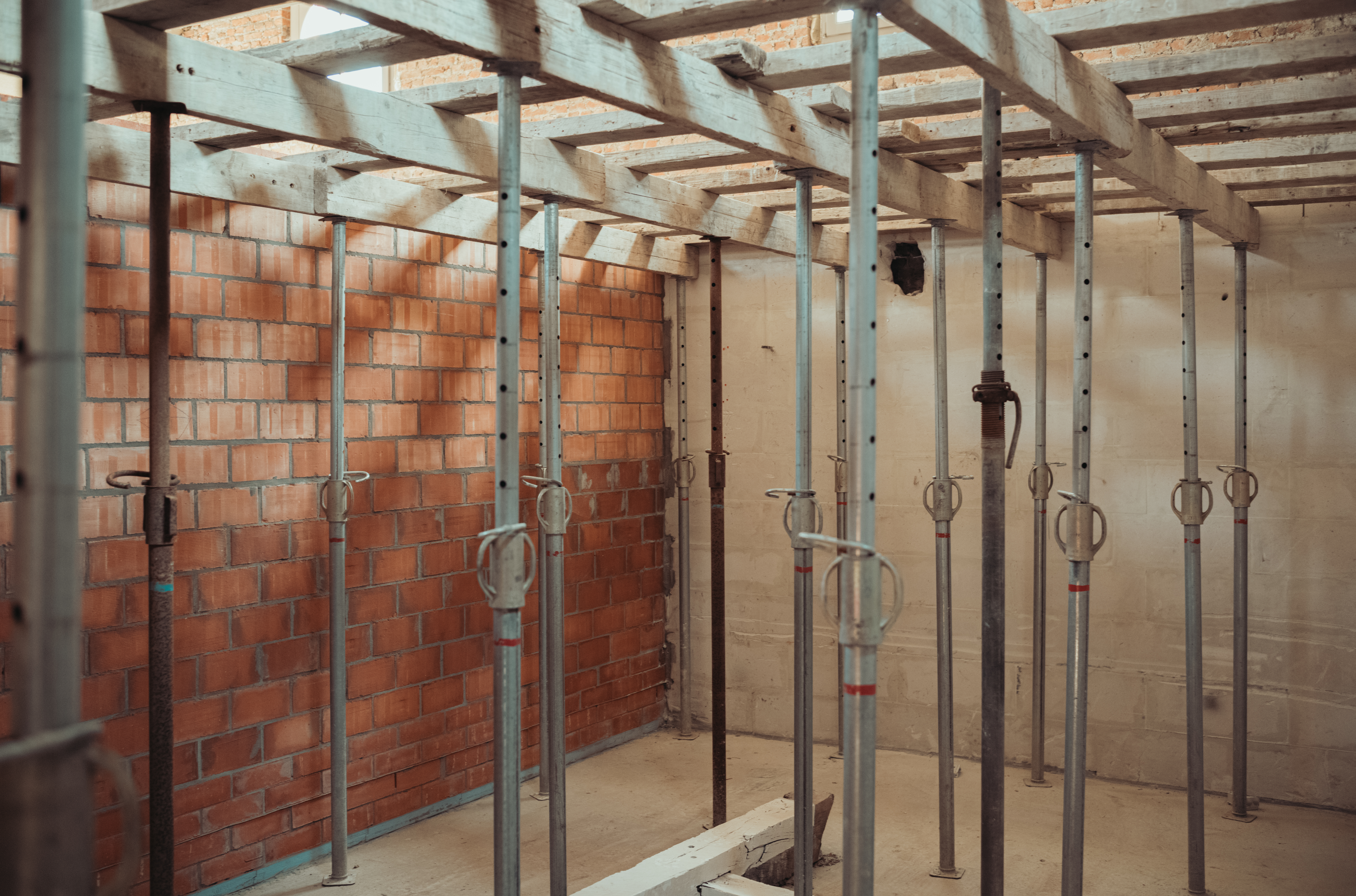 Metal support poles hold up wooden beams in preparation for pouring a new concrete floor in the building.