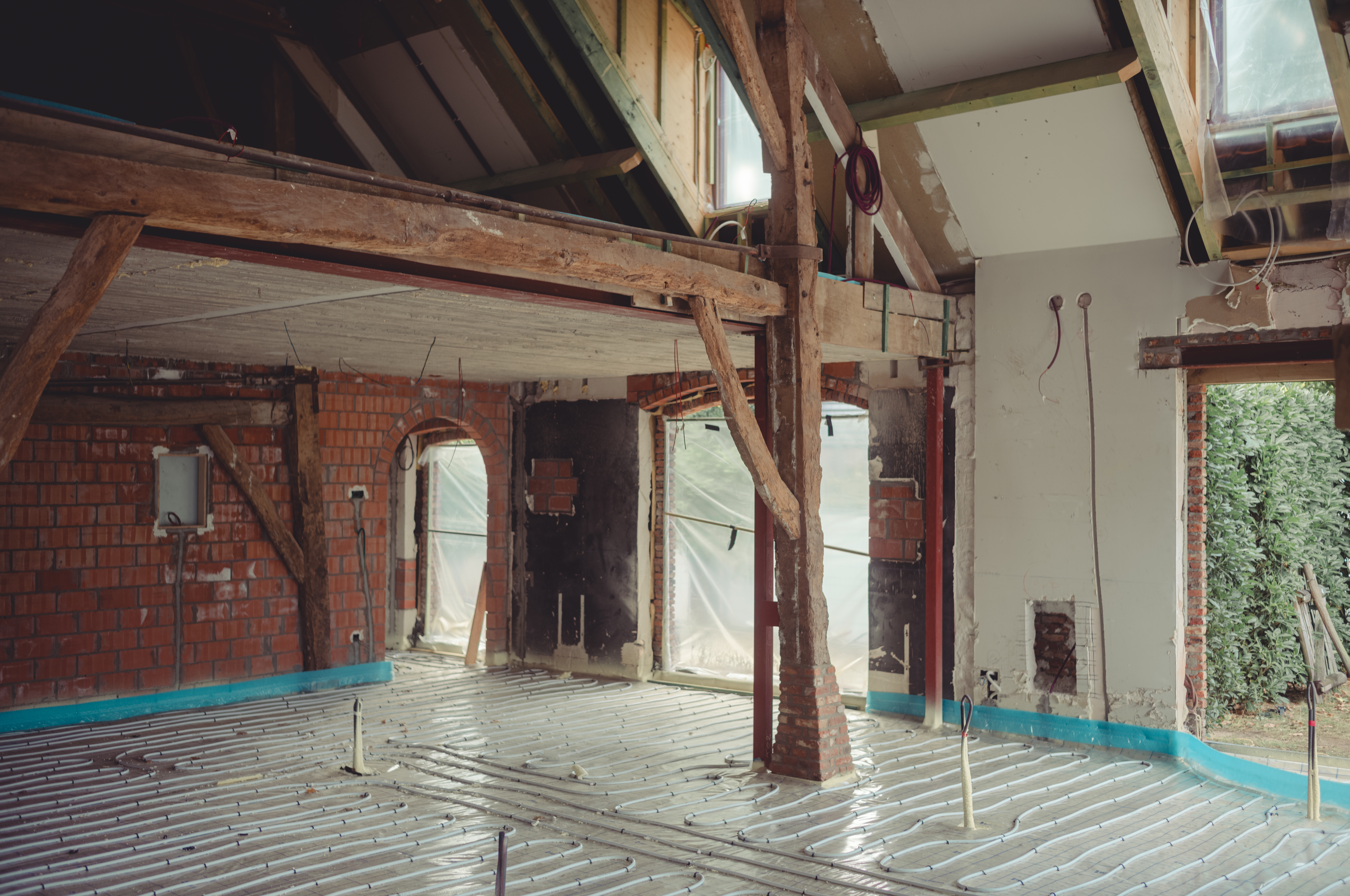 Underfloor heating is being installed in a renovated living room with exposed beams and unfinished walls.