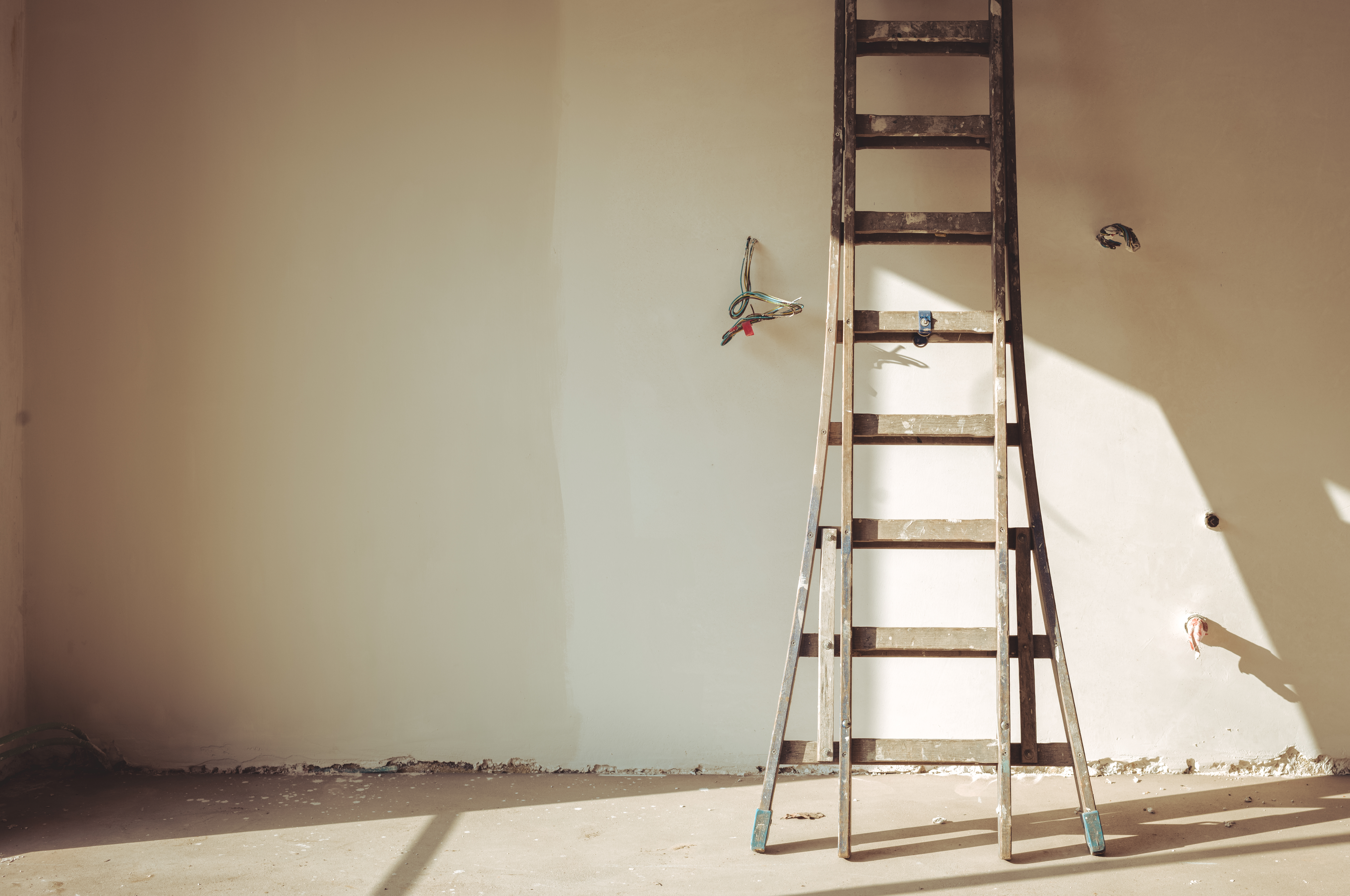 A wall with two paint colors on it and a ladder leaning against it.