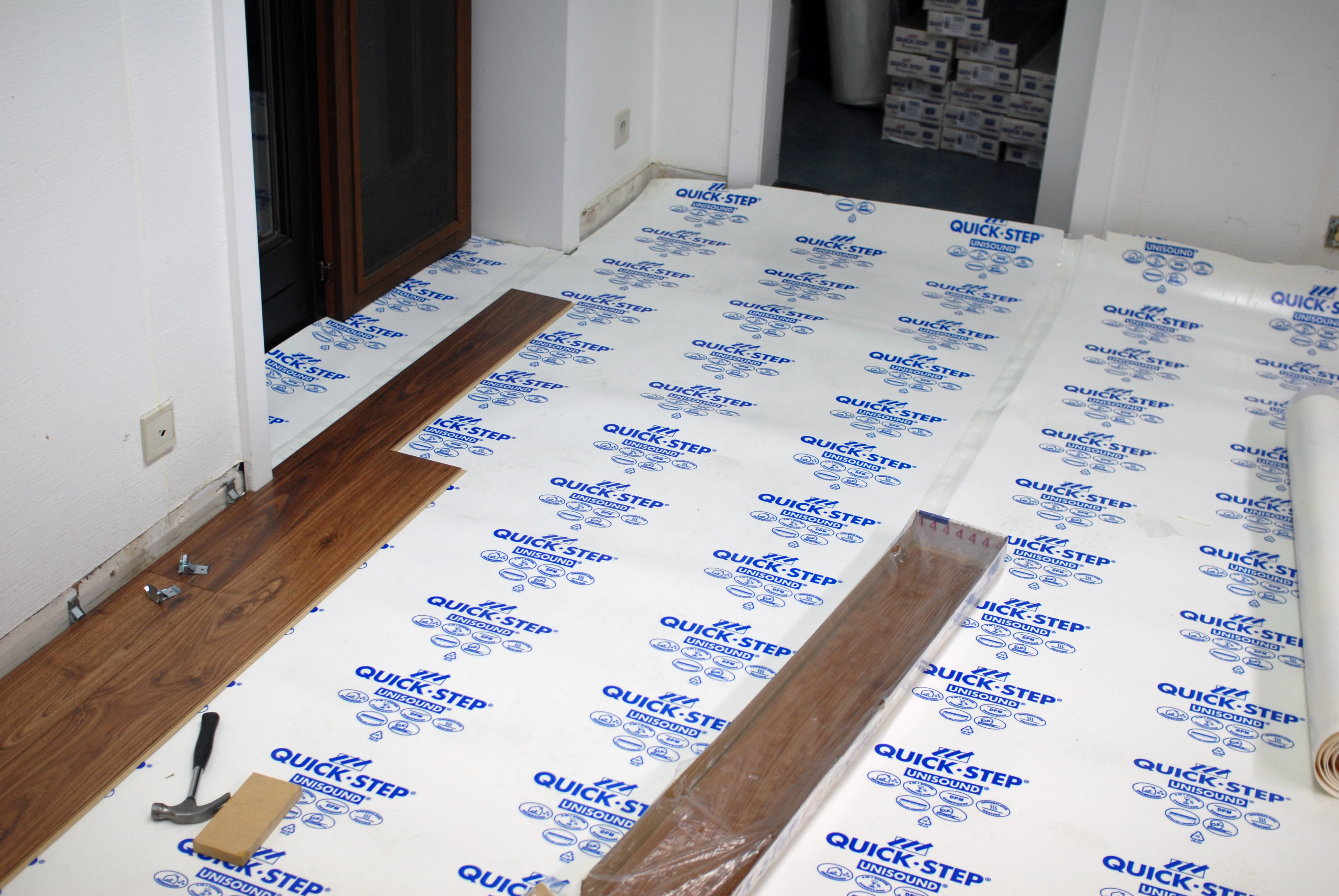 Partially installed wooden flooring in an office, with tools and materials scattered on a protective underlayment.
