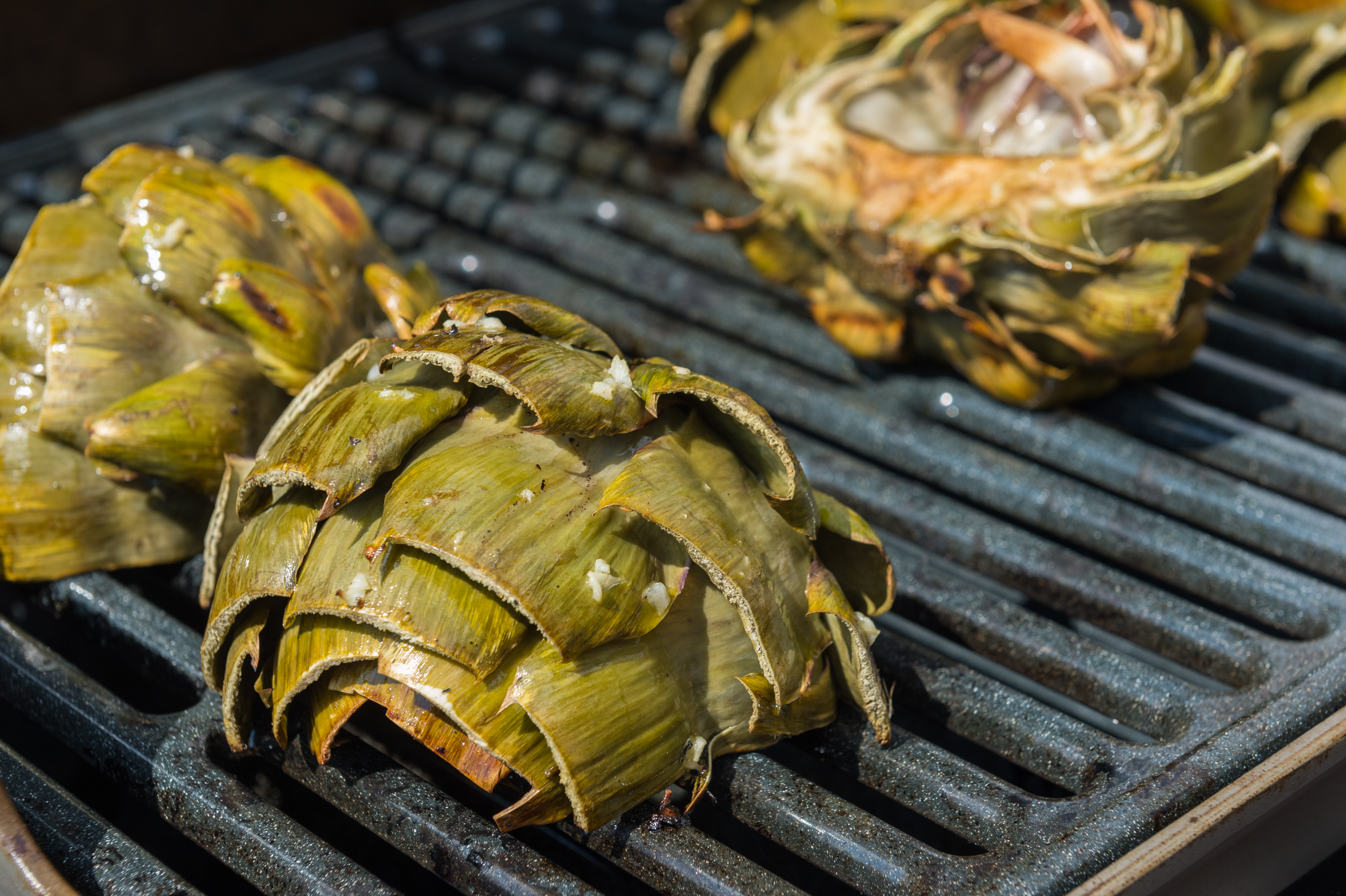 Artichokes cooking on a grill, with some cut open and seasoned.